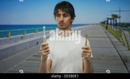 Man holds electric toothbrush in one hand and wooden toothbrush in the other on street; confusion decision dilemma. Stock Photo