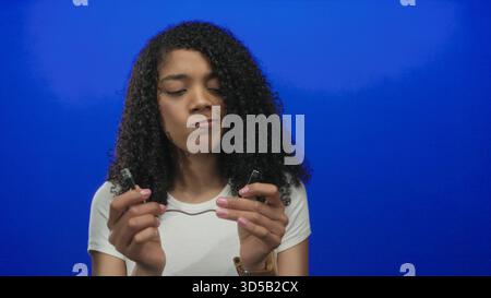 African american woman holding a broken usb cable with hands in a vibrant blue studio; frustration connection failure. Stock Photo