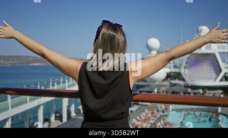 Woman standing with outstretched arms and hands on railing on cruise deck overlooking pool and sea; serenity travel escape. Stock Photo