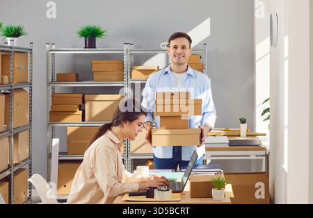Woman working on laptop in warehouse checking stock and inventory with male coworker. Stock Photo