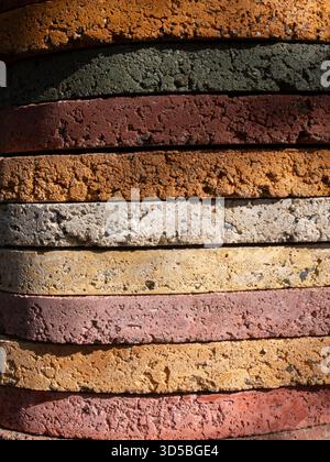 Close-up of stacked concrete paver rings in warm earthy colors and one green band, showing rough porous texture and alternating horizontal layers. Stock Photo