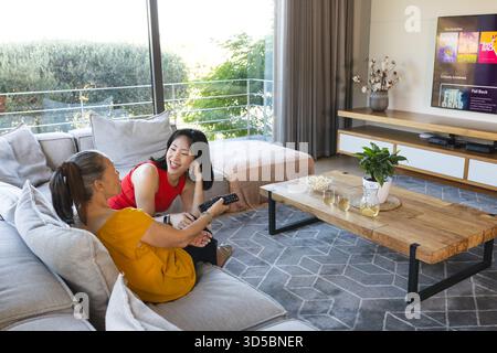 Women relaxing on sofa, watching TV and enjoying snacks in modern living room Stock Photo