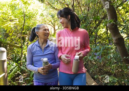 Asian senior mother and daughter walking in park, holding water bottles, smiling together Stock Photo