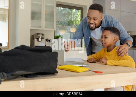 Father and son using laptop at home, learning together with smiles Stock Photo