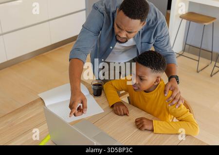 Father helping son with homework on laptop at home, pointing at screen Stock Photo