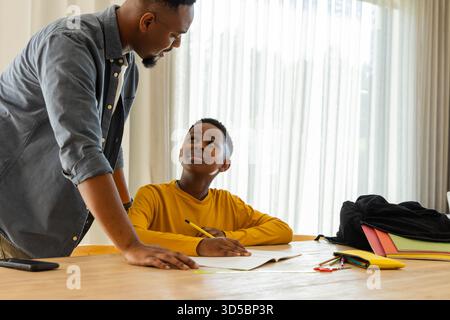 Father helping son with homework at table, both smiling and engaged Stock Photo