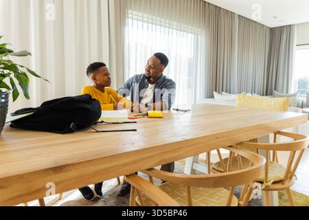Father and son doing homework together at home, smiling and bonding Stock Photo
