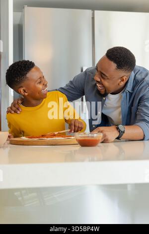 Father and son making pizza together in kitchen, sharing joyful moment Stock Photo