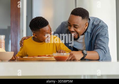 Father and son making pizza together in kitchen, sharing laughter and joy Stock Photo