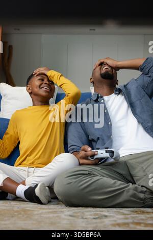 African American father and son laughing together while playing video games on couch at home Stock Photo