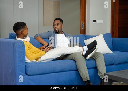 African American African American father and son relaxing on sofa, talking and using digital tablets Stock Photo