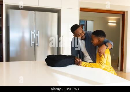 African American father and son playing mini golf in modern kitchen with black backpack Stock Photo