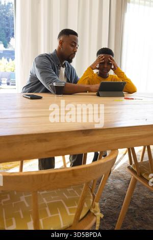 Father helping son with homework on tablet at home, both concentrating Stock Photo
