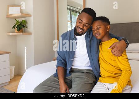 Father and son sitting on bed, embracing and smiling at home Stock Photo