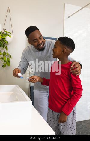Father helping son brush teeth in bathroom, sharing joyful morning routine Stock Photo