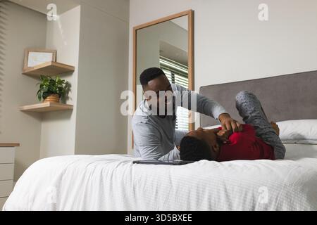 African American father and son playing on bed in modern bedroom, with tablet on edge Stock Photo