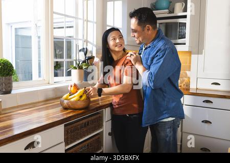 Asian couple in kitchen sharing affectionate moment while preparing fresh fruit Stock Photo