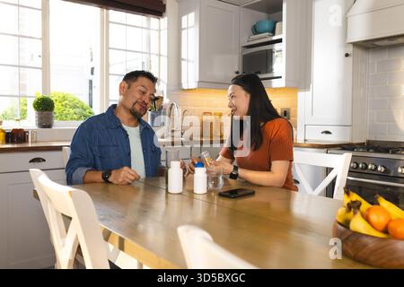 Mature Asian couple enjoying breakfast together at kitchen table, sharing joyful moment Stock Photo