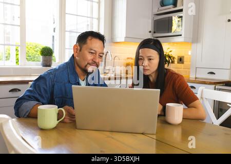 Asian couple using laptop at home, drinking coffee, and focusing on screen Stock Photo