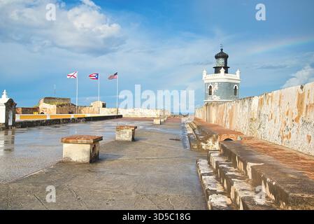 A coastal fort features a lighthouse against a bright blue sky with a faint rainbow. Stock Photo