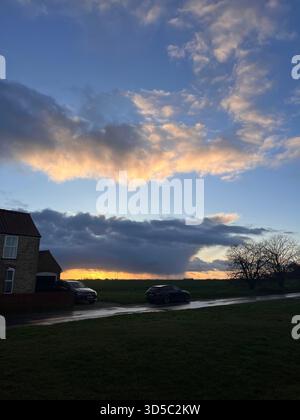 Dark storm clouds rolling over a quiet suburban road with parked cars during golden sunset in Hull, England. Stock Photo