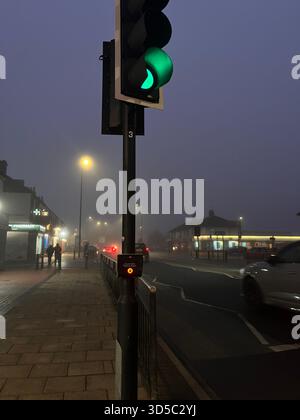 Green traffic light glowing through dense fog on a quiet urban street in Hull, England, with soft bokeh lights and misty early morning atmosphere. Stock Photo