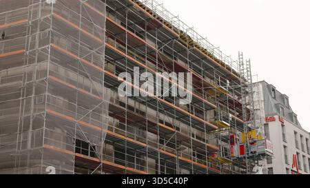 Workers are busy at a construction site, surrounded by scaffolding and machinery in a city area on a cloudy day. Stock Photo