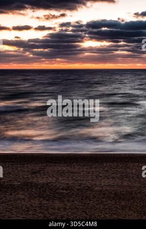 Long-exposure sunrise with smooth blurred waves, warm horizon colors and dramatic clouds above the Black Sea in Obzor, Bulgaria. Calm atmospheric coas Stock Photo