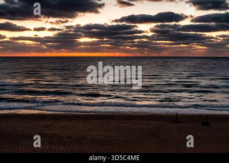 Dramatic sunrise above the Black Sea with layered clouds, soft orange horizon light and empty sandy beach in Obzor, Bulgaria. Peaceful seascape with w Stock Photo