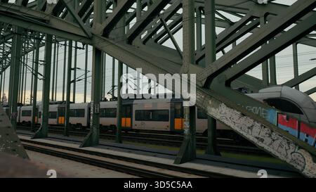 Trains move under a large green bridge, showcasing urban life as the sky darkens at dusk. Stock Photo