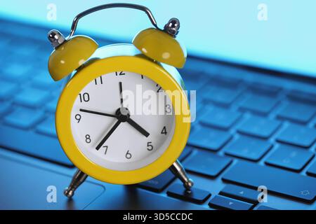 Yellow alarm clock on a laptop computer keyboard. Online business deadline, networking time management and daily business tasks planning concept. Stock Photo
