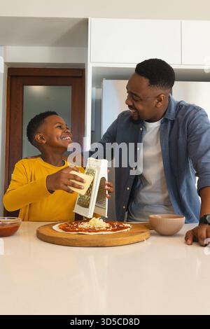 Father and son making pizza together, grating cheese and sharing laugh Stock Photo