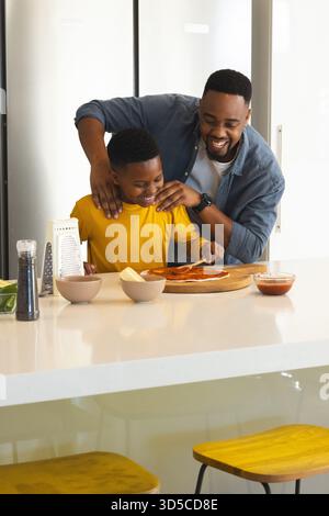 Father and son making pizza together in kitchen, sharing joyful moment Stock Photo