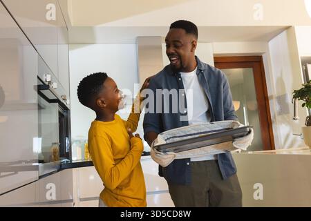 Father and son bonding in kitchen, smiling while baking together at home Stock Photo