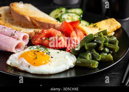 English breakfast - fried egg, ham, green beans, tomatoes, cucumbers and toast. Stock Photo