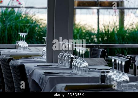 A table set with white wine glasses is ready for restaurant guests to enjoy lunch outdoors in good weather. Stock Photo