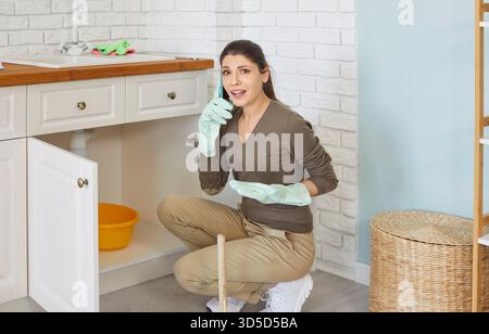 Need help with kitchen sink clogged, woman complaining by phone on household problem, pipes blockage Stock Photo