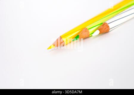 A close-up, low-angle shot of the sharpened tips of yellow, green, and white colored pencils against a bright white background. Stock Photo