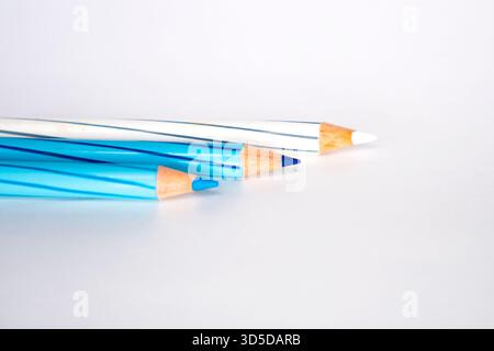 Three striped colored pencils, featuring shades of blue and white, are resting diagonally on a white background. The focus is on the sharpened tips. Stock Photo