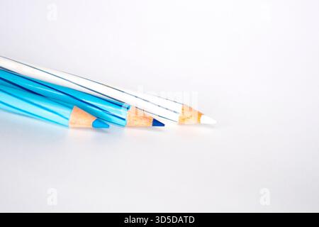 Three striped colored pencils, featuring shades of blue and white, are resting diagonally on a white background. The focus is on the sharpened tips. Stock Photo
