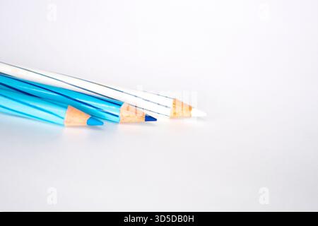 Three striped colored pencils, featuring shades of blue and white, are resting diagonally on a white background. The focus is on the sharpened tips. Stock Photo