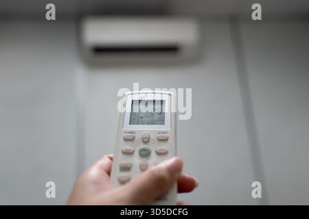 Hand Holding Air Conditioner Remote Control Set to 25 Degrees Celsius in AUTO Mode Stock Photo