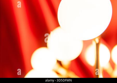 A soft-focus, abstract shot of warm, bright globe lights against a rich red curtain backdrop, creating an elegant and vibrant mood. Stock Photo