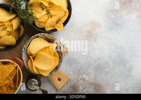 Snacks. Unhealthy food. All classic potato snacks with peanuts, popcorn and onion rings and salted pretzels in bowl plates on gray concrete background. Unhealthy food for figure, heart, skin, teeth Stock Photo