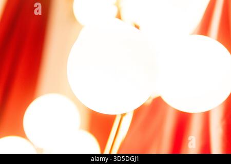 A soft-focus, abstract shot of warm, bright globe lights against a rich red curtain backdrop, creating an elegant and vibrant mood. Stock Photo