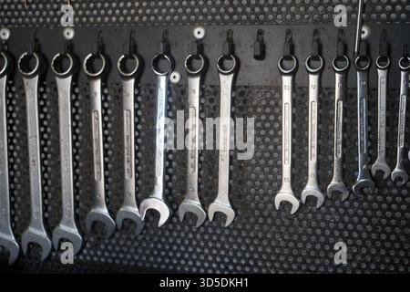 A precise close-up of a row of shining silver wrenches hanging neatly on a workshop pegboard, illustrating organization and readiness. Stock Photo