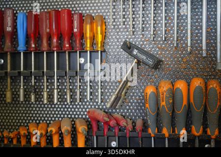 A dynamic shot of various hand tools, including screwdrivers, hex keys, and a T-handle wrench, covered in sawdust on a workshop pegboard. Stock Photo
