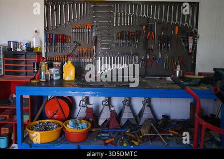A wide shot of an organized workshop wall with various hanging metal tools and a workbench with equipment. Stock Photo