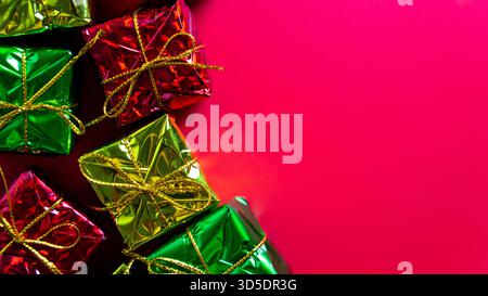 A shiny green, red, and gold wrapped gift boxes with gold strings sits against a red background. Christmas, holiday celebrations or sales events. Stock Photo