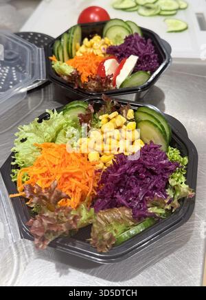 Colorful fresh salad served in black plastic bowls includes grated carrots, sweet corn, red cabbage, lettuce, and sliced cucumbers. Pro Photo Stock Photo